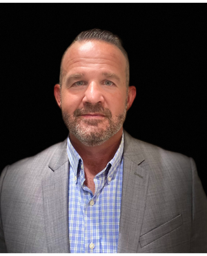 Ryan McMillian | SMC A photo of a man in a grey suit and blue checkered shirt.